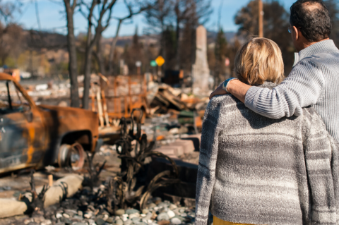 Couple standing in front of their burned down home.