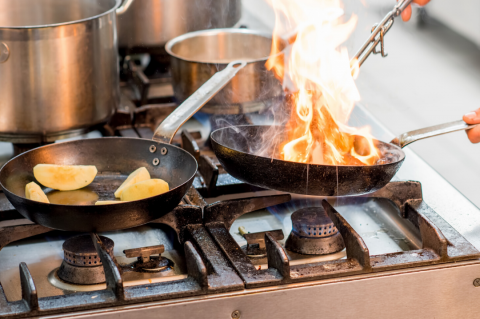 Person cooking over a gas stove with potatoes in one pan and a fire flame in another pan.