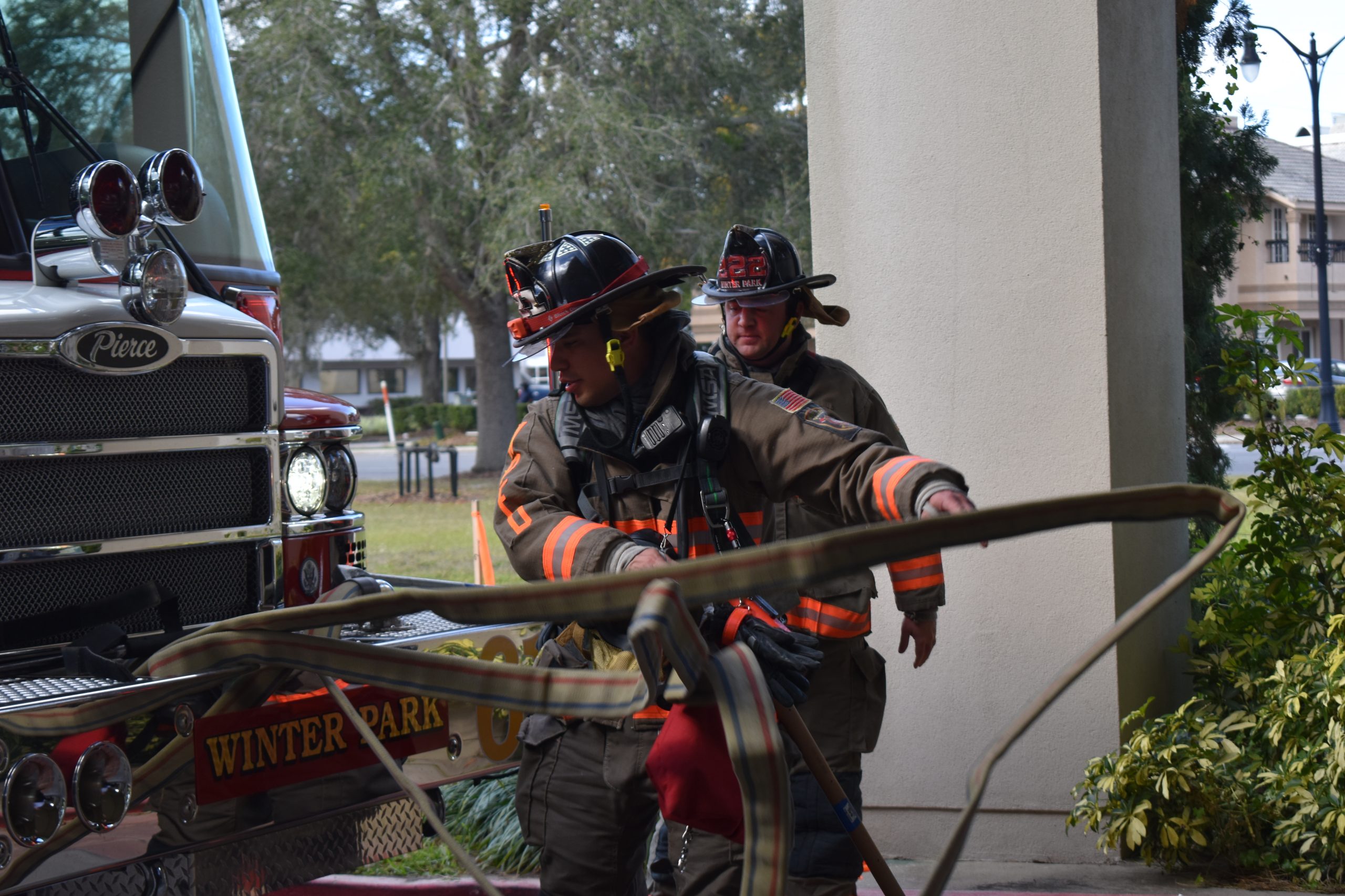 Two firefighters unloading hose from the front of the engine.