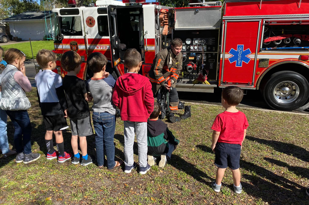 Firefighter addressing a group of young children beside a fire truck about fire safety.