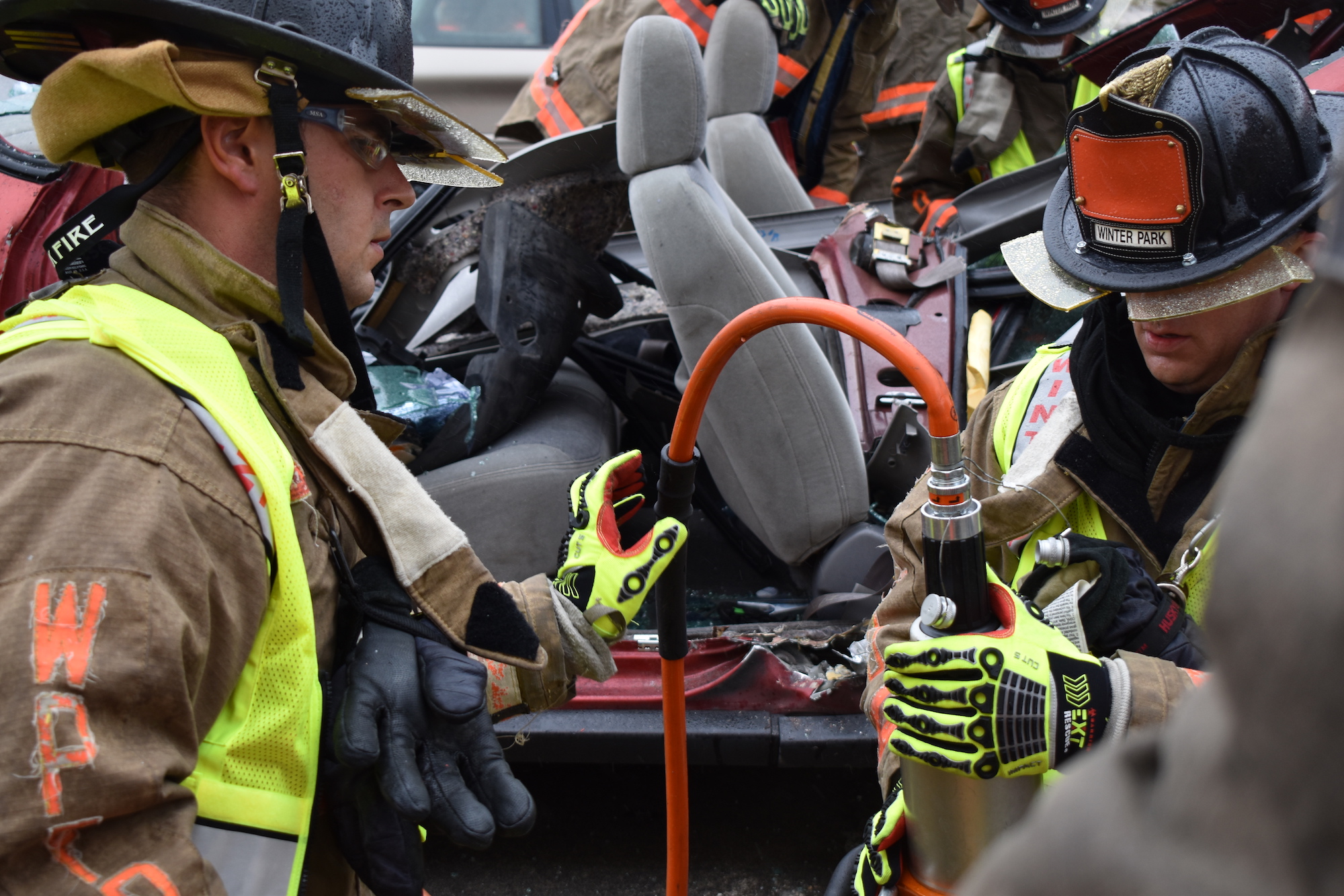 Two firefighters working with extrication tools during training in front of a cut up vehicle.