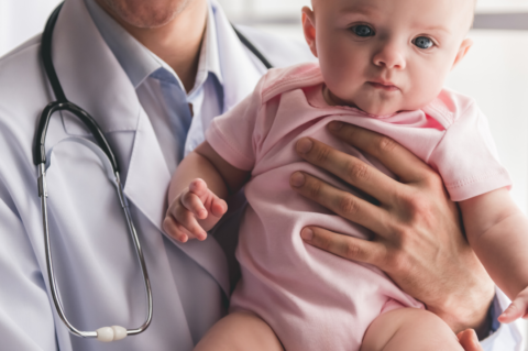 Doctor holding baby sitting up with stethoscope