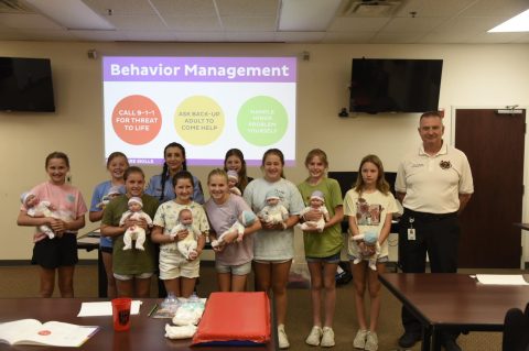 Group picture of instructor with children holding training props used for CPR.