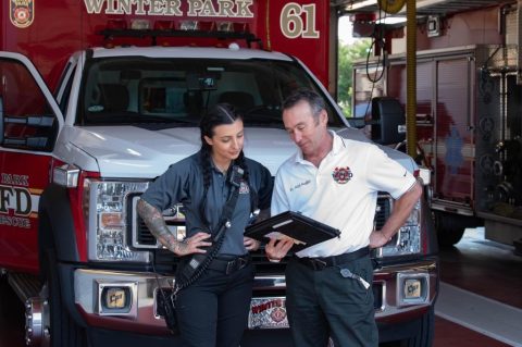 Medical director looking at an iPad and a firefighter stand in front of fire ambulance