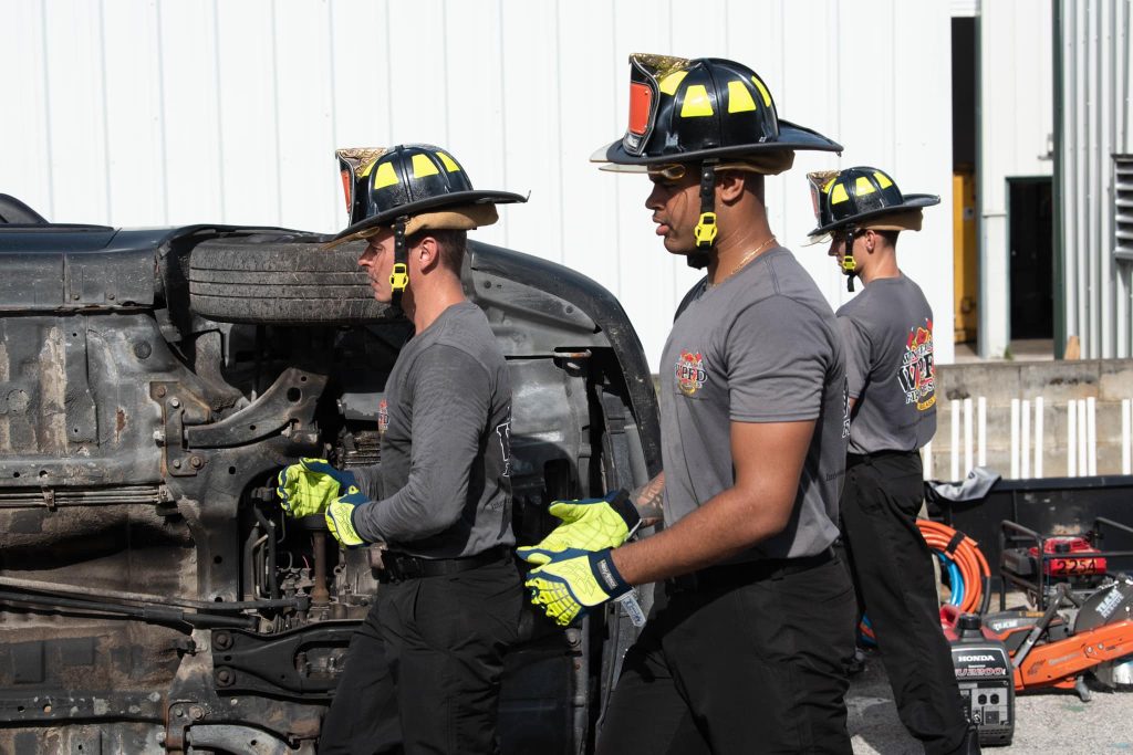 Firefighters with helmets and gloves by a vehicle on its side.