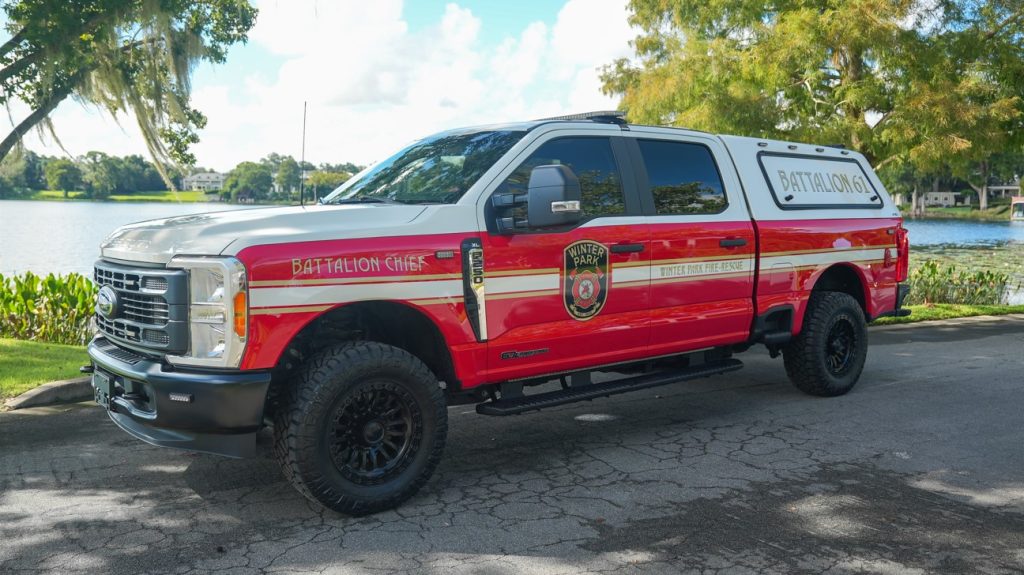 Battalion 61 parked on the street in front of a lake and trees.